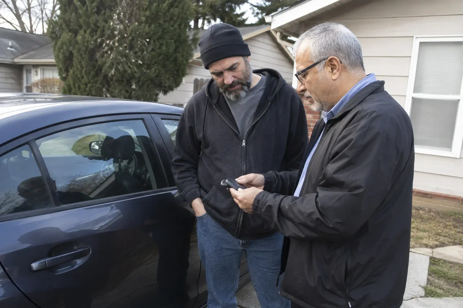 Two adults discussing a key fob beside a parked car. — Car Lockout Service, Milton