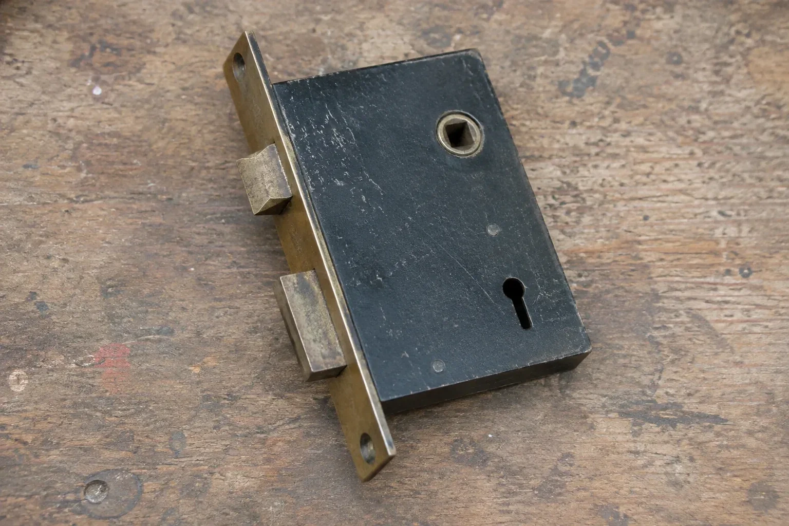 Closed mortise lock case with spindle opening, keyhole, latch and deadbolt on a wooden workbench. — Vintage Mortise Lock Service, Milton